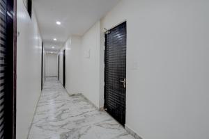 a corridor with white walls and marble floors and a black door at FabHotel Metro Inn in Kānpur
