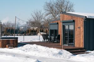 a small cabin with a wooden deck in the snow at Derylovka - domki, jacuzzi, sauna in Zamość