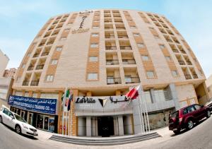 un grand bâtiment avec des voitures garées devant lui dans l'établissement La Villa Inn Hotel Apartments, à Doha