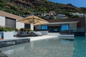a house with a swimming pool and an umbrella at Villa Anjos - Luxury Villa with Infinity Pool & Ocean View in Canhas