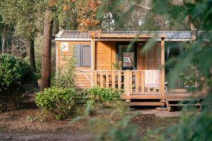 a wooden cabin with a porch in the woods at Camping LANDAE in Ondres