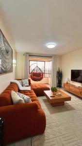 a living room with two orange couches and a television at Midtown LakeView 2BR House with Heated pool, Netflix, 24Hr security & reception -Shawmut Nakuru in Nakuru