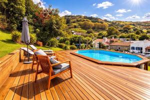 a wooden deck with a pool and chairs and an umbrella at Casa do Priolo - Villaverde Azores in Feteiras