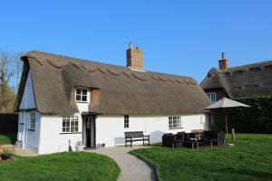 a thatched cottage with a bench and an umbrella at The Elm, Abbots Ripton in Abbots Ripton