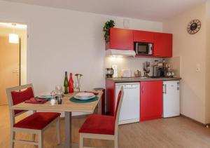 a small kitchen with red cabinets and a table with chairs at Zenao Appart'hôtels Strasbourg in Strasbourg +3 photos
