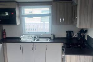 a kitchen with white cabinets and a sink and a window at Caravan- Sleeps 6 2 Bedrooms - Thurston Manor in Dunbar +5 photos