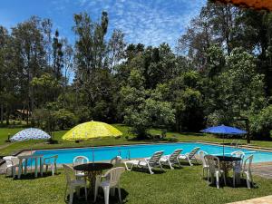 Eine Gruppe von Stühlen und Tischen mit Sonnenschirmen neben einem Pool in der Unterkunft Hotel Refazenda in Visconde De Maua