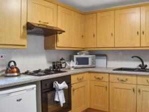 a kitchen with wooden cabinets and a stove top oven at Byre Cottage - Uk50028 in Liskeard