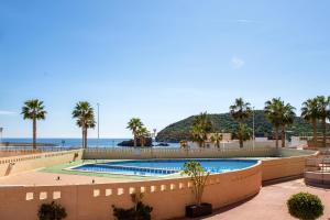 a swimming pool with palm trees and the ocean at Apto Primera Línea con Piscina - Guipas Beach in Puerto de Mazarrón