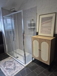 a shower with a glass door and a picture on a cabinet at Sleep Eat Repeat Apartment in Macclesfield