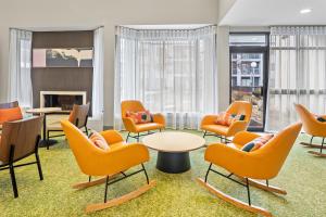 a waiting room with orange chairs and tables and a fireplace at Spark by Hilton Bettendorf Quad Cities in Bettendorf