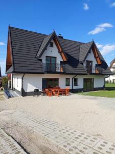 a white house with a black roof and wooden tables at Koperkowe Domki Zakopane in Zakopane