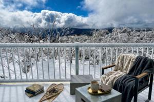 a chair and a table on a balcony with snow at Mount Buller Alpine Chalet Mountain Views Sleeps up to 12 in Mount Buller