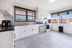 a large kitchen with white cabinets and windows at Jack & Bias Cottage in Warrnambool +9 photos