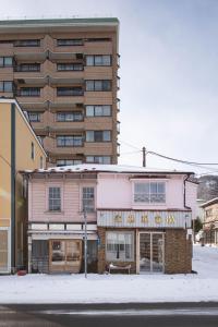 a pink building on a street with a tall building at 佐藤理容Inn in Hakodate