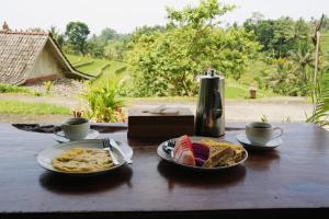 a wooden table with two plates of food and cups at D'Ume Bendoel Homestay in Jatiluwih +125 photos