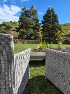 two wicker chairs and a bench in a garden at Blue Aster Retreat in Mokau