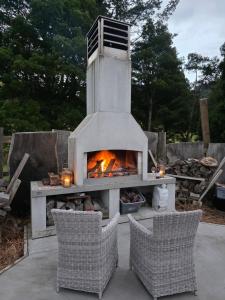a outdoor oven with two chairs and a fireplace at Blue Aster Retreat in Mokau
