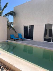 a swimming pool with two blue chairs next to a house at La Belle Dojo in Chelem