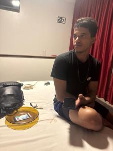 a man sitting on a bed holding a cell phone at Clt in Brasília