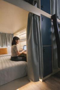 a woman sitting on a bed with a laptop at Faloe Hostel in Kota Kinabalu