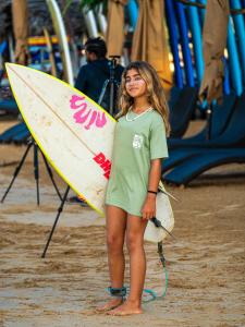 a young girl standing on the beach holding a surfboard at Secret Surf Hostel in Weligama