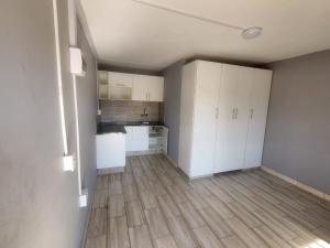 an empty kitchen with white cabinets and a wooden floor at AMASHIYA flats in Richards Bay
