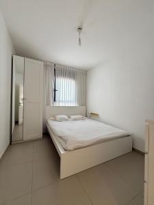 a white bedroom with a bed and a window at שלוות העמק - דירת 3 חדרי שינה במיקום מרכזי in Ganne Tiqwa