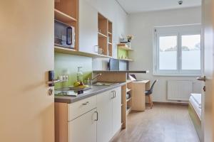 a small kitchen with white cabinets and a desk at I AM HOTELS Leoben in Leoben