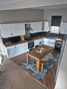 a kitchen with white cabinets and a wooden table at Sleep Eat Repeat Apartment in Macclesfield