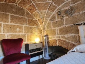 a bedroom with a stone wall with a bed and a chair at Casa Cassiano in Patù