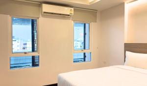 a bedroom with three windows and a bed with white sheets at Paul and Pam Hotel Bangkok in Bang Kapi