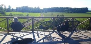 two women sitting on chairs on a porch with a view of a field at Pensionat på hästgård in Alunda +2 photos