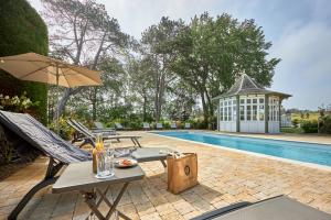 Eine Terrasse mit Stühlen und einem Sonnenschirm neben einem Pool in der Unterkunft Les Villas d'Arromanches, Teritoria in Arromanches-les-Bains