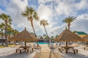 a beach with tables and straw umbrellas and palm trees at Island House 1Bu By Pkrm in Pensacola