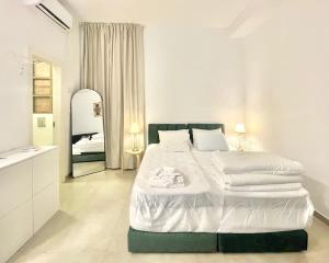 a white bedroom with a large bed and a mirror at Nachlaot Gem - Bright, Central and Cozy in Jerusalem