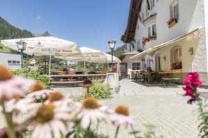 eine Terrasse mit Tischen, Sonnenschirmen und Blumen in der Unterkunft Posthotel Strengen am Arlberg in Strengen