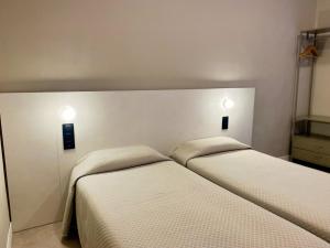 two beds in a bedroom with two lights on the wall at Pensión Coral in Barcelona