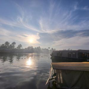 a boat on a river with the sun reflecting on the water at Sacred River Houseboats in Alleppey