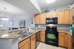a kitchen with wooden cabinets and black appliances at 5 Star Resort 2BR 2 BATH King Suite Shuttle Pools Across from Beach 2208 in Destin
