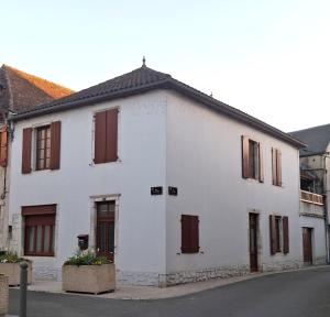 a white building with brown shutters on a street at La maison de Lau in Salies-de-Béarn