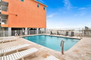 a swimming pool with chairs and a building at Gulf Shores Barefoot Bliss in Gulf Shores