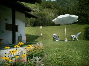 an umbrella and chairs and flowers in a yard at Casa Davide Valdaone in Daone