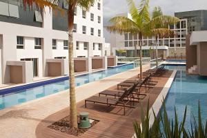 an image of a swimming pool with chairs and palm trees at Flat moderno Jade hotel in Brasília