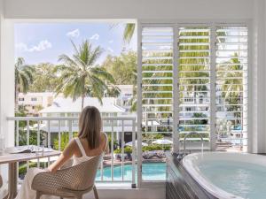 a woman sitting in a chair on a balcony overlooking a swimming pool at Peppers Beach Club & Spa in Palm Cove