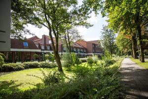 una pasarela a través de un jardín con árboles y edificios en Hotel Ostfriesen Hof, en Leer