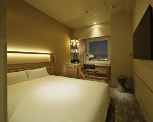 a bedroom with a bed and a desk and a window at Candeo Hotels Chino in Chino