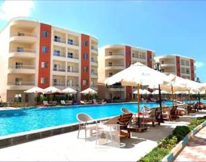 a swimming pool with chairs and umbrellas next to buildings at Modern Luxury Villa Steps from the Sea North Coast in Borg El Arab