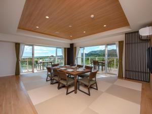 a dining room with a table and chairs and windows at Lieta Nakayama in Nago