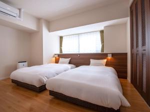 two beds in a bedroom with white sheets and a window at Lieta Nakayama in Nago